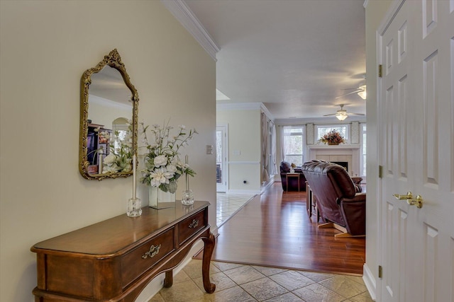 tiled foyer with a fireplace, ceiling fan, and crown molding