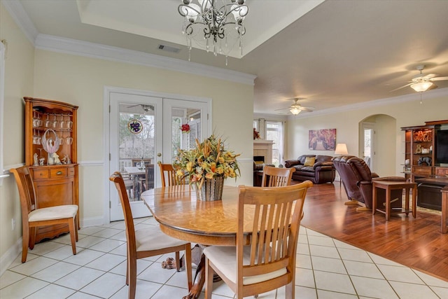 tiled dining area with a raised ceiling, crown molding, french doors, and ceiling fan with notable chandelier