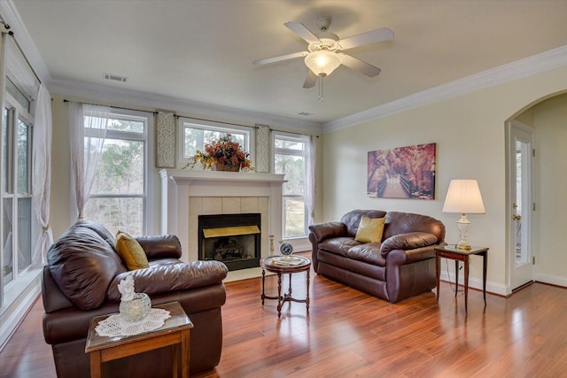 living room featuring a tile fireplace, crown molding, plenty of natural light, and ceiling fan