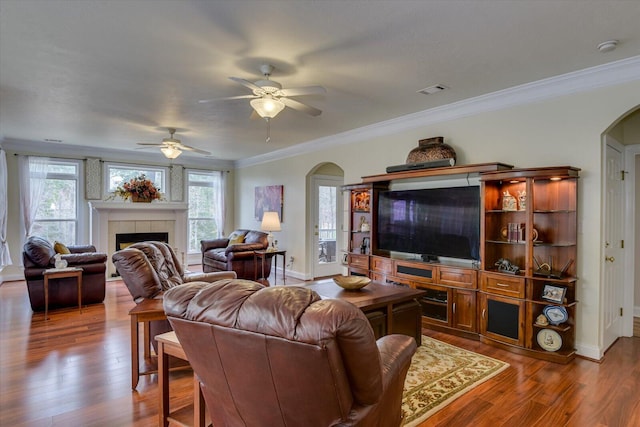 living room featuring a tile fireplace, dark wood-type flooring, ceiling fan, and ornamental molding