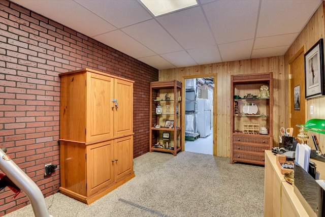 interior space featuring wooden walls, a drop ceiling, light colored carpet, and brick wall