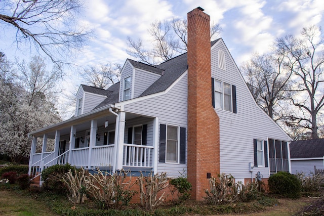 view of side of property with a porch, roof with shingles, and a chimney