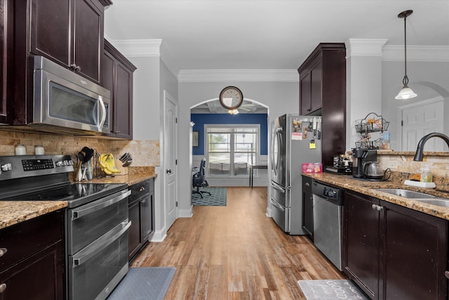 kitchen featuring arched walkways, a sink, light wood-type flooring, light stone countertops, and stainless steel appliances