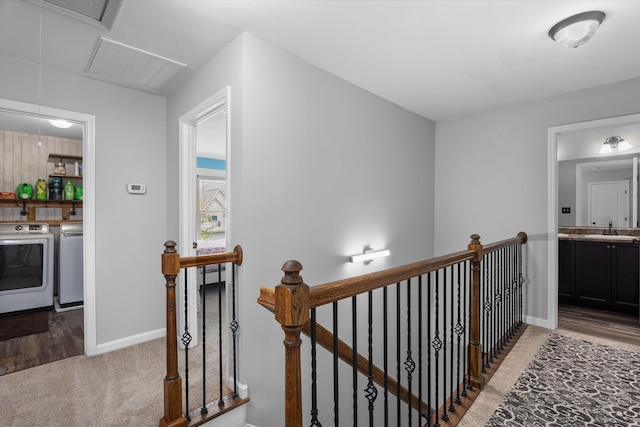 corridor featuring baseboards, a sink, an upstairs landing, attic access, and washing machine and dryer