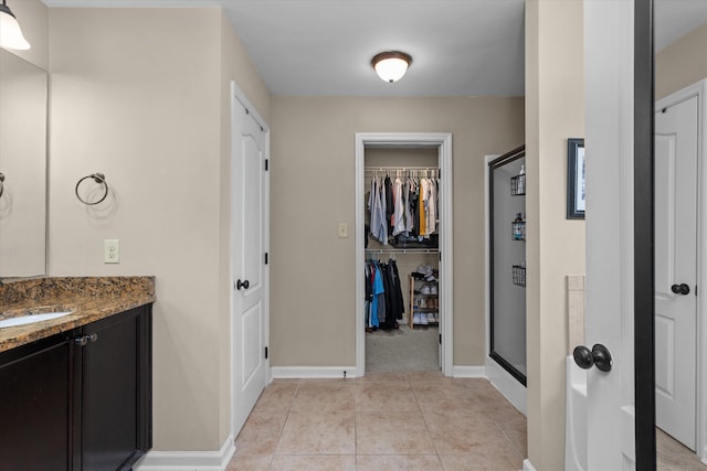 full bathroom featuring vanity, baseboards, tile patterned floors, a shower stall, and a walk in closet
