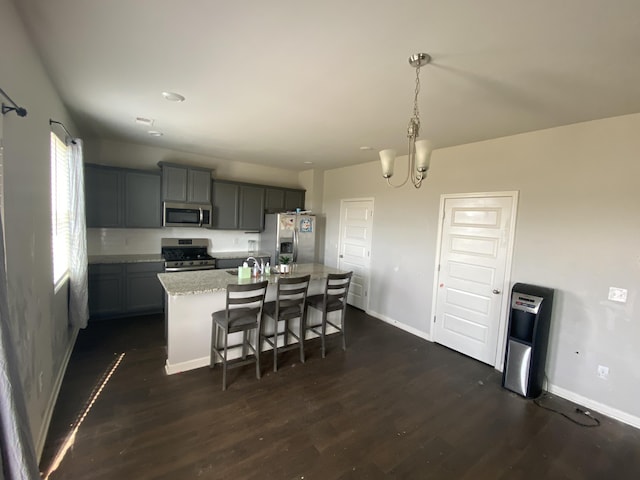 kitchen featuring a kitchen island with sink, stainless steel appliances, baseboards, dark wood finished floors, and decorative light fixtures