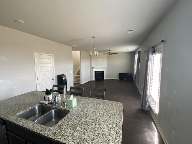 kitchen featuring stone counters, a fireplace, a sink, visible vents, and an island with sink