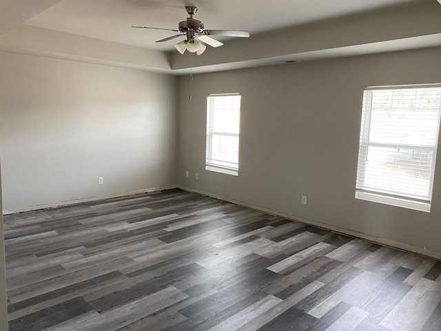 empty room with ceiling fan, a tray ceiling, and dark wood-type flooring