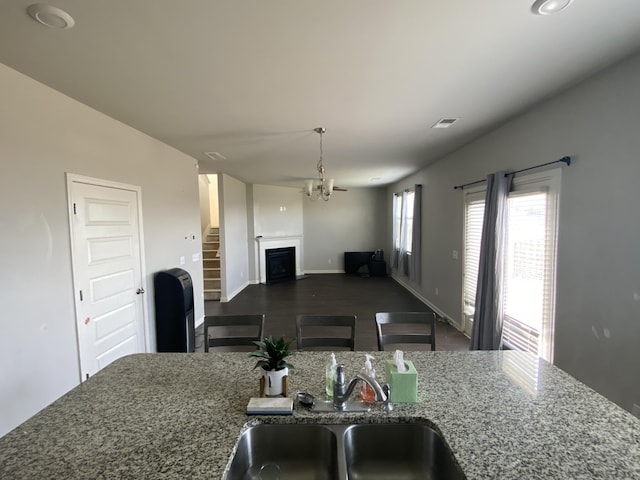 kitchen featuring a fireplace, visible vents, open floor plan, a sink, and dark stone countertops