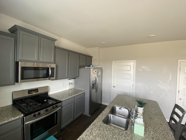 kitchen featuring stone counters, dark wood-style flooring, a sink, appliances with stainless steel finishes, and gray cabinets