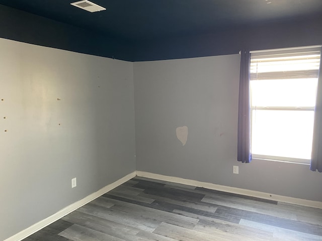 unfurnished room with visible vents, plenty of natural light, baseboards, and wood finished floors