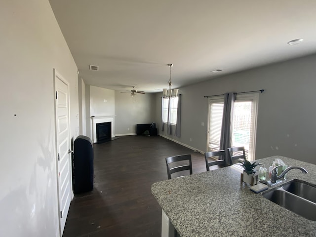 kitchen featuring baseboards, visible vents, dark wood-style flooring, a fireplace, and a sink