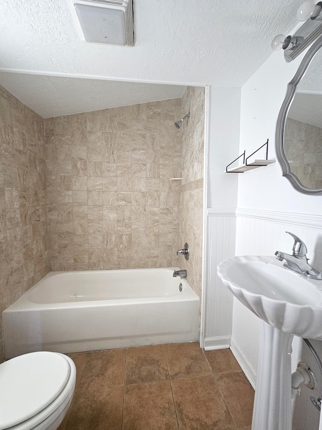 bathroom with tiled shower / bath combo, tile patterned floors, a textured ceiling, and toilet