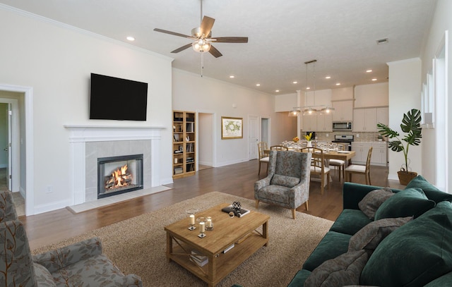 living area with wood finished floors, ornamental molding, a tile fireplace, a ceiling fan, and baseboards