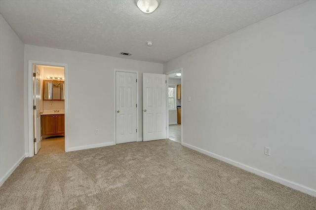 unfurnished bedroom featuring light colored carpet, connected bathroom, and a textured ceiling