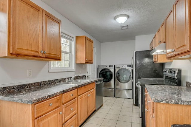 kitchen featuring appliances with stainless steel finishes, sink, light tile patterned floors, washing machine and clothes dryer, and a textured ceiling