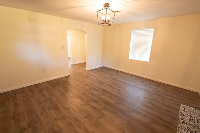 unfurnished room with baseboards, arched walkways, and dark wood-style floors