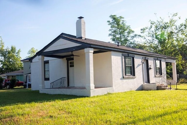 back of property with stucco siding, a chimney, a lawn, and ceiling fan