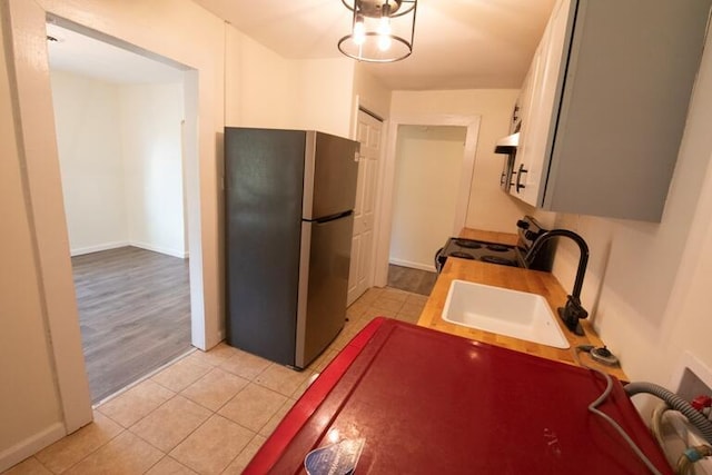 kitchen featuring a sink, freestanding refrigerator, light tile patterned floors, baseboards, and electric stove