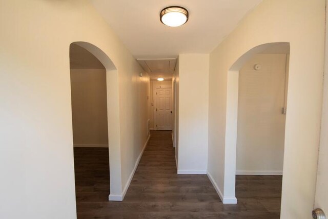 corridor featuring baseboards, arched walkways, attic access, and wood finished floors
