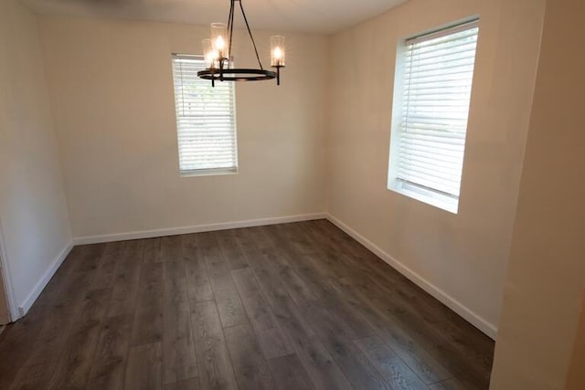 empty room featuring plenty of natural light, dark wood-style flooring, and a notable chandelier