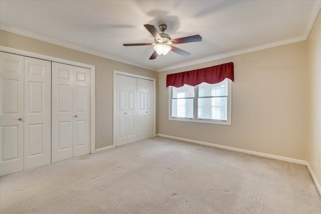 unfurnished bedroom with carpet floors, crown molding, baseboards, and two closets