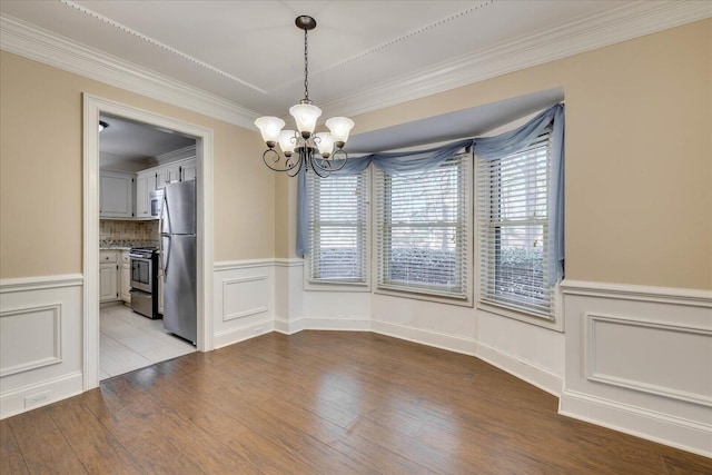 unfurnished dining area featuring ornamental molding, a wainscoted wall, a notable chandelier, and wood finished floors