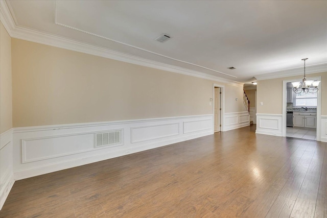 spare room featuring a sink, wood finished floors, visible vents, an inviting chandelier, and crown molding