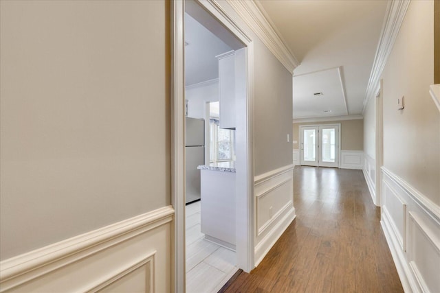 corridor with french doors, crown molding, a decorative wall, and wood finished floors