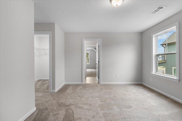 unfurnished bedroom featuring a spacious closet, light colored carpet, and a closet