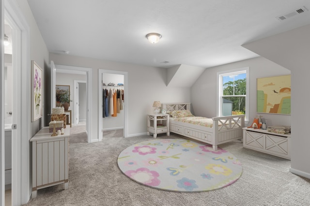 bedroom with ensuite bathroom, a walk in closet, light carpet, and a closet