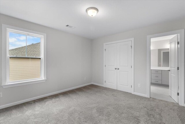 unfurnished bedroom featuring a closet, ensuite bath, and light carpet