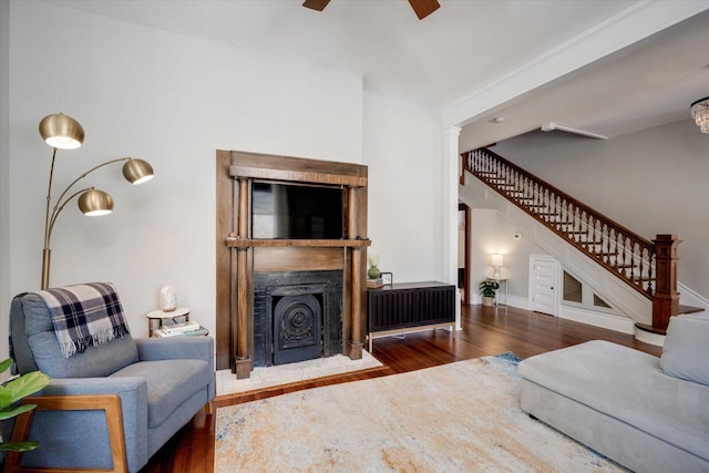 living room with stairs, a fireplace with flush hearth, wood finished floors, and a ceiling fan