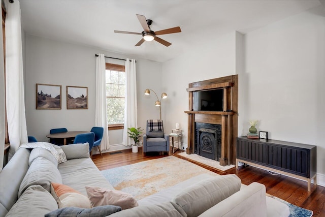 living area featuring wood finished floors, baseboards, visible vents, a ceiling fan, and a fireplace