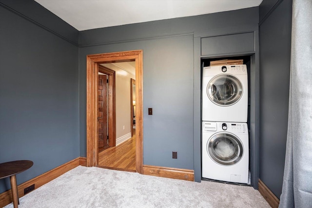 clothes washing area with baseboards, carpet floors, and stacked washer and dryer