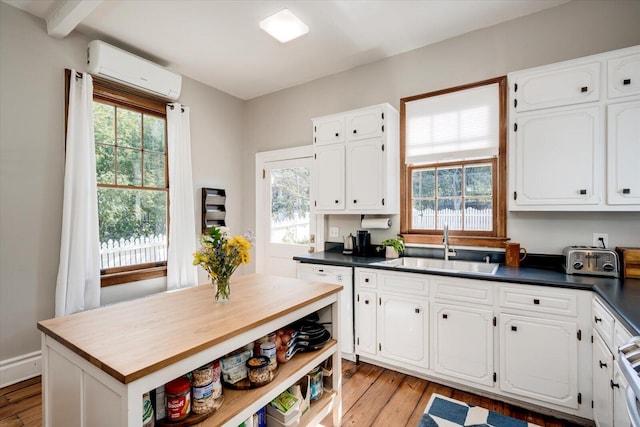 kitchen featuring a wall unit AC, white cabinetry, light wood-style floors, and a sink