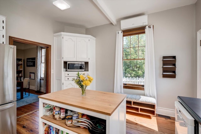 kitchen with white cabinetry, a wall unit AC, appliances with stainless steel finishes, and hardwood / wood-style floors