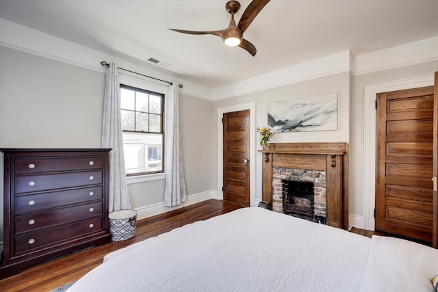 bedroom featuring visible vents, dark wood-type flooring, ceiling fan, baseboards, and a stone fireplace