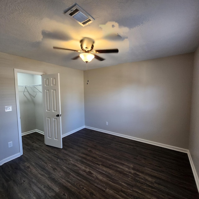 unfurnished bedroom featuring visible vents, a closet, baseboards, a walk in closet, and dark wood finished floors