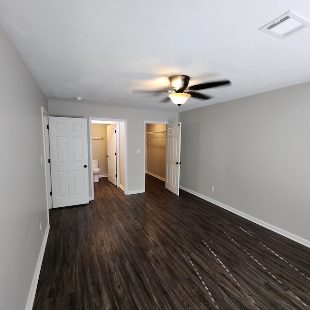 unfurnished bedroom featuring baseboards, dark wood finished floors, a spacious closet, and visible vents