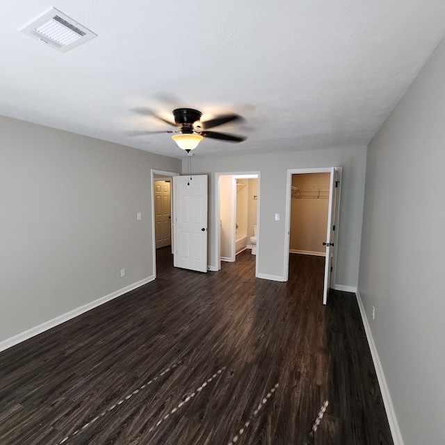 unfurnished bedroom with a walk in closet, dark wood-style flooring, visible vents, baseboards, and a closet