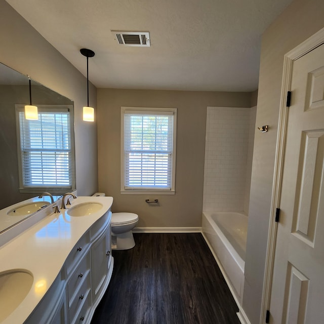 full bathroom featuring visible vents, double vanity, wood finished floors, toilet, and a sink