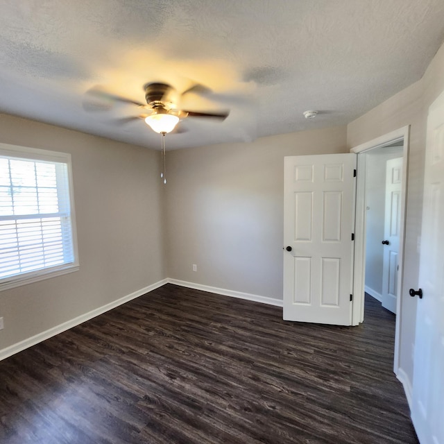 empty room with dark wood-type flooring, a ceiling fan, baseboards, and a textured ceiling