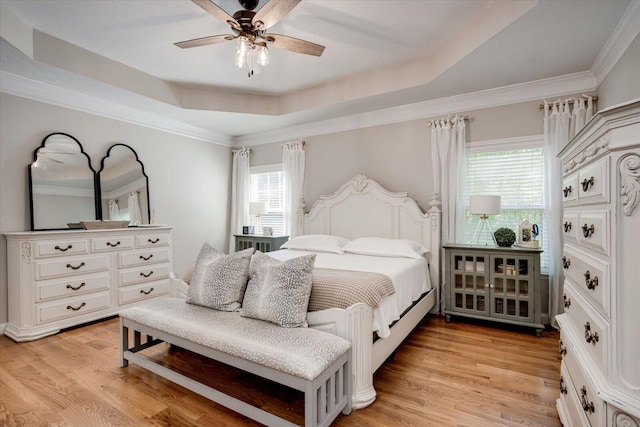 bedroom featuring ceiling fan, multiple windows, light wood-style flooring, and a raised ceiling