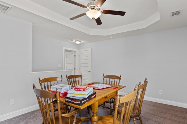 carpeted dining area with a tray ceiling and ceiling fan