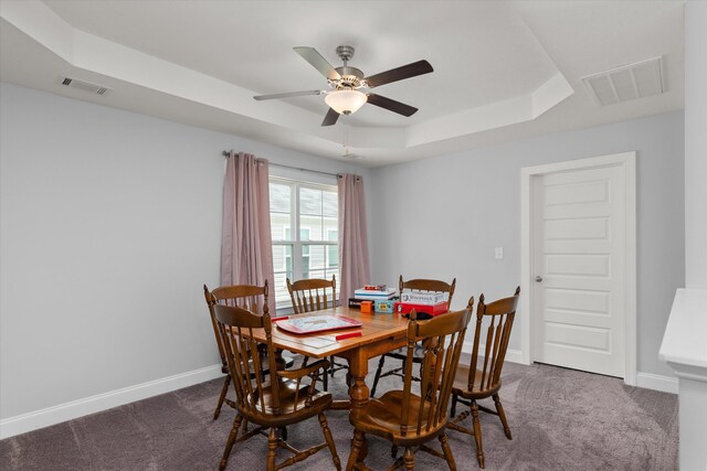 dining space with dark colored carpet, a tray ceiling, and ceiling fan