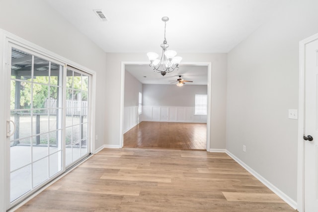 unfurnished dining area with ceiling fan with notable chandelier, a wealth of natural light, and light hardwood / wood-style flooring