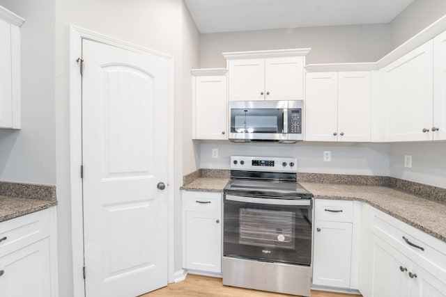 kitchen featuring light stone counters, white cabinets, stainless steel appliances, and light wood-type flooring