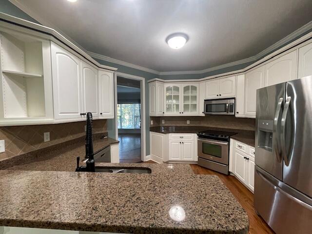 1212 Sumter Landing Ln, Evans, GA 30809 - kitchen with stainless steel appliances, a peninsula, dark stone counters, white cabinetry, and crown molding