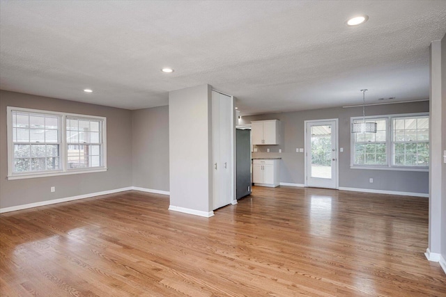 unfurnished living room with recessed lighting, baseboards, light wood-type flooring, and a textured ceiling